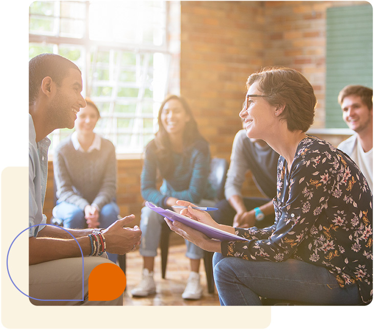 Two people talking happily while sitting in a large group therapy session.