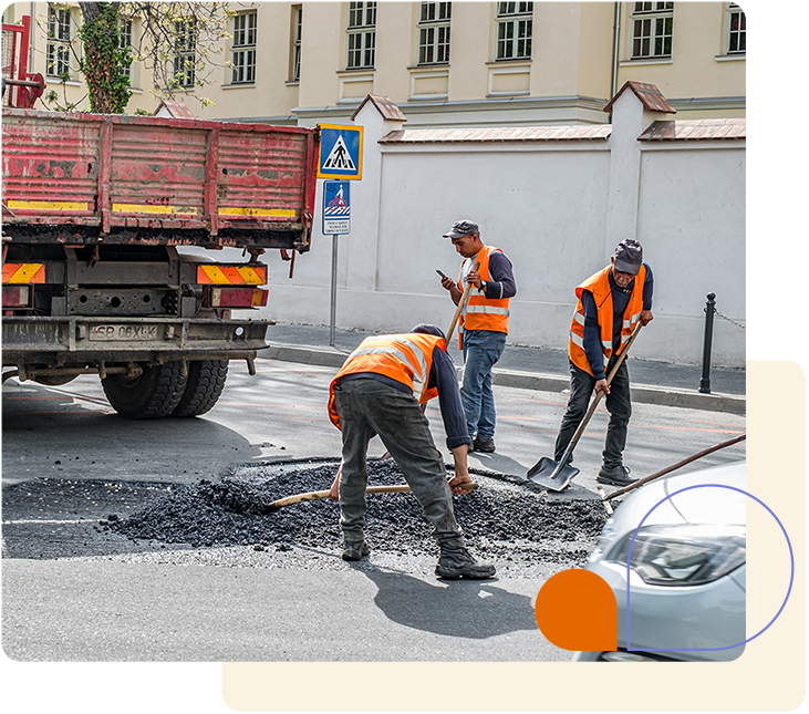 A group of three construction workers repairing a road with major cracks and potholes.
