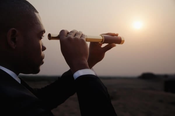 Young businessman looking through telescope in the the desert